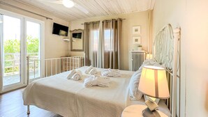 Ein Hotelzimmer mit Bett, Nachttischlampe, einem Fenster mit Vorhängen, Heizkörper und einem Fernseher an der Wand.