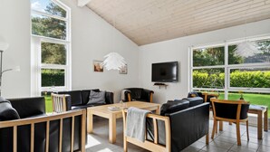 Un salon moderne doté d’un grand téléviseur, de sièges confortables et de grandes fenêtres donnant sur le jardin.