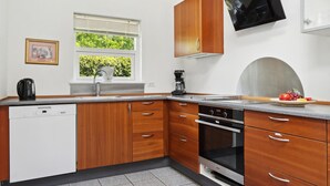 Une cuisine moderne avec des meubles en bois, un four encastré et une fenêtre donnant sur un paysage verdoyant.