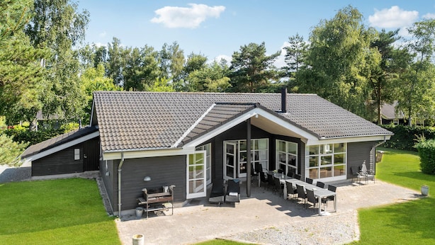 Une maison moderne dotée d’un toit en pente, de grandes fenêtres et d’un patio aménagé avec du mobilier d’extérieur.