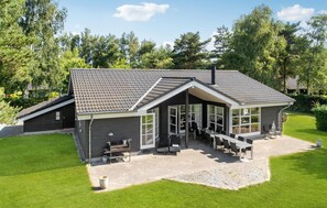 Moderni talo, jossa on kalteva katto, suuret ikkunat ja patio, jossa on ulkokalusteita.