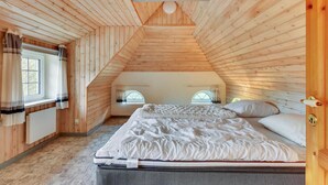 Une chambre confortable située dans les combles, avec des murs en bois, un plafond en pente et un lit recouvert de linge de maison blanc.