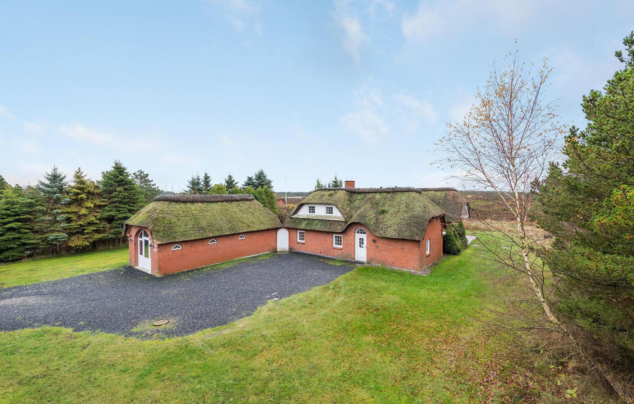 A traditional thatched-roof house with a gravel driveway and a grassy lawn.
