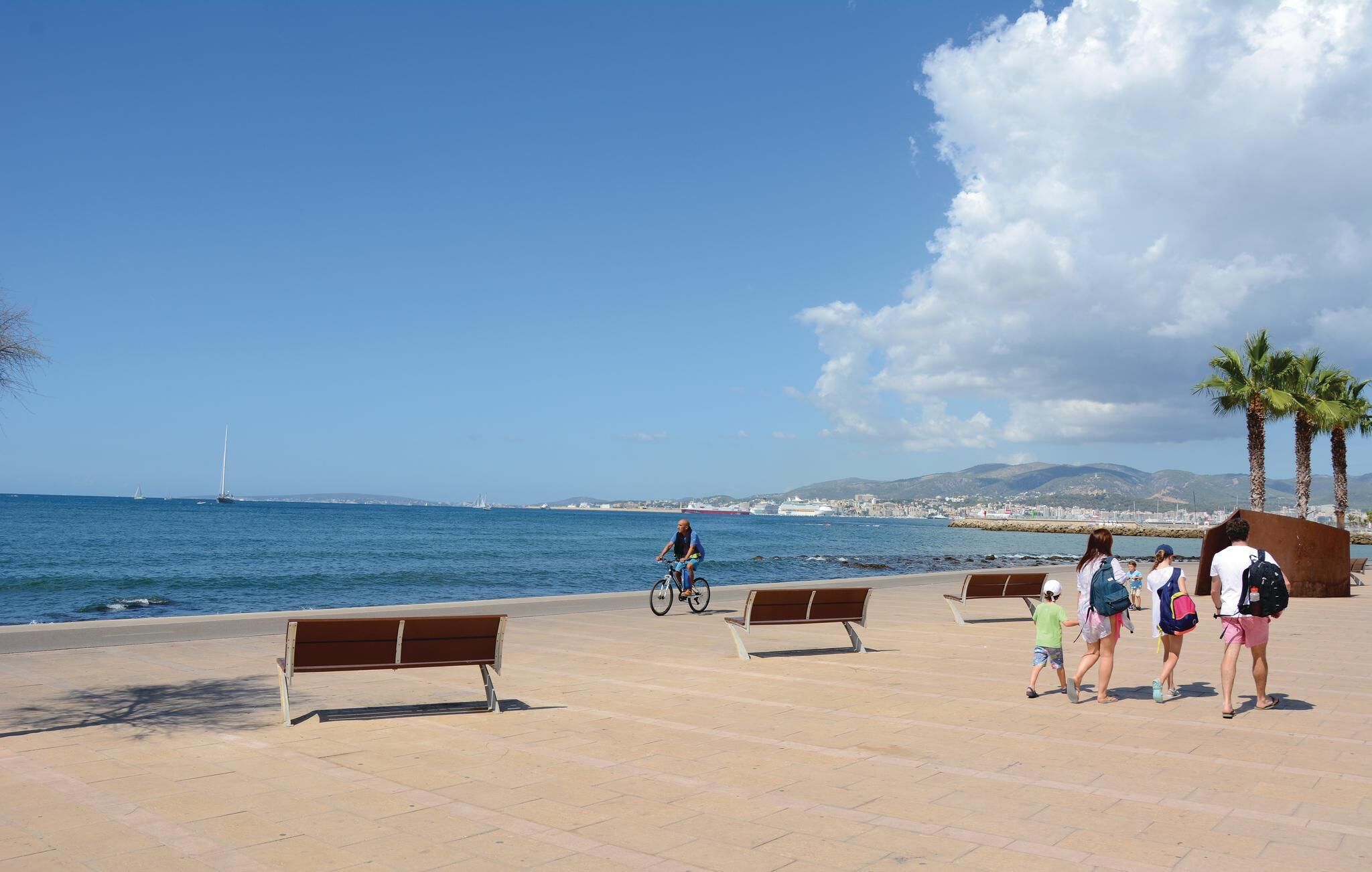 Une promenade en bord de mer, avec des bancs, un cycliste et un groupe de personnes qui se promènent.