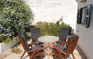 Une terrasse avec une table ronde et quatre chaises, entourée d’un mur blanc et d’un arbuste aux fleurs bleues.