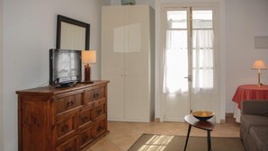 A living room with a wooden cabinet, a television, a small table with a bowl, a sofa, and a door with curtains.
