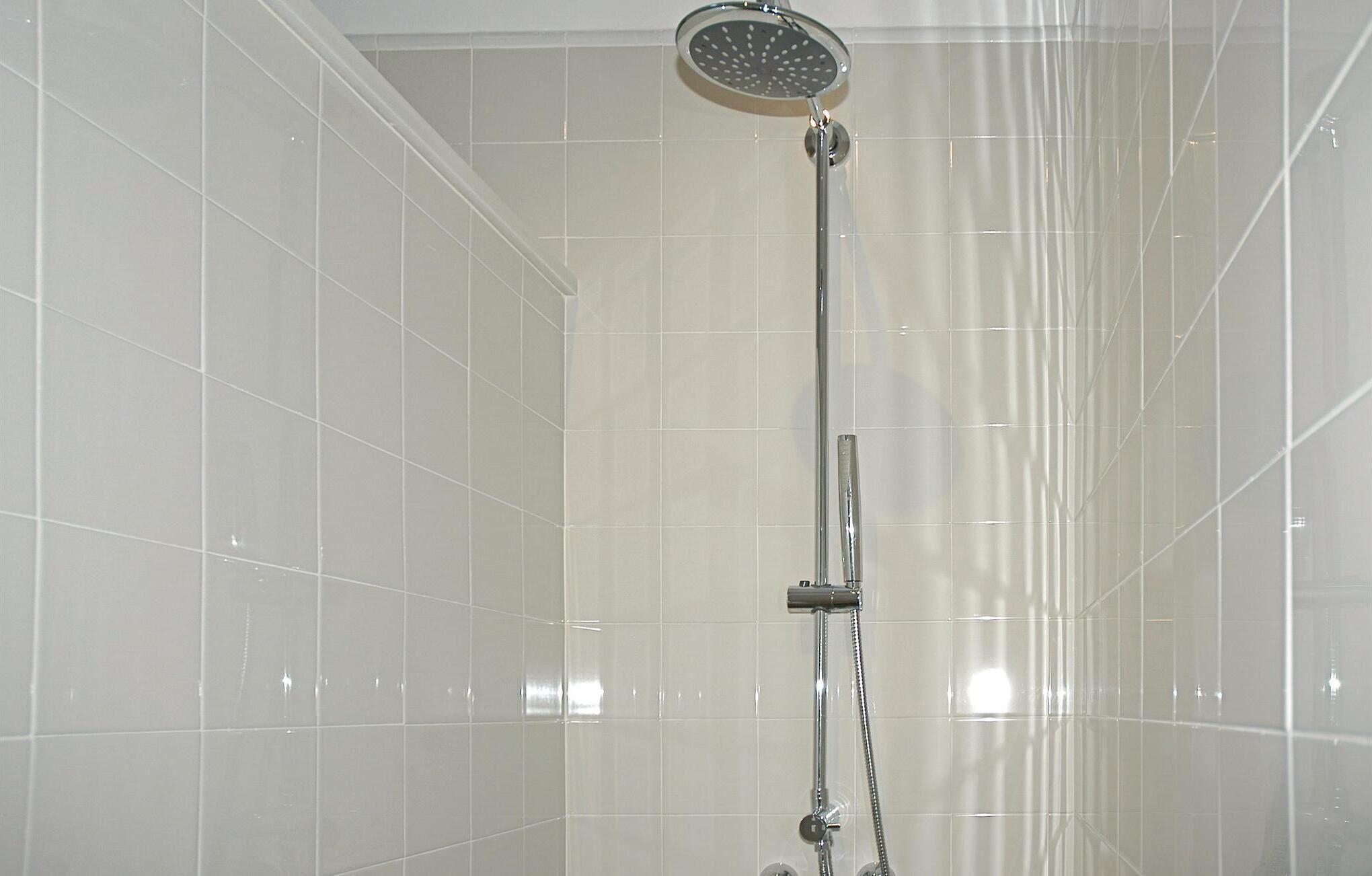 Une douche équipée d’un pommeau de douche à main et d’un robinet mural.