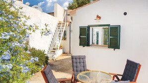 A patio with a table and chairs, a window with shutters, and a ladder leading to a higher level.