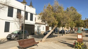 A street scene with a bench, parked cars, a building with shutters, and a tree.