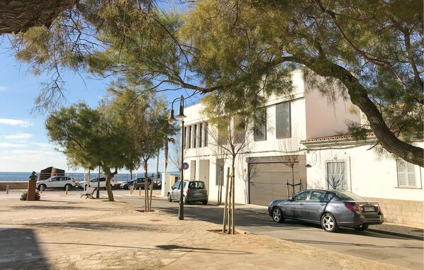 Une rue côtière bordée de voitures garées, un immeuble avec un portail de garage et des arbres.