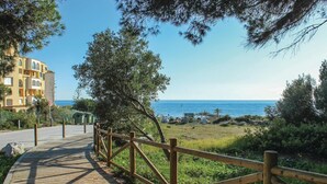 Un sentiero lastricato conduce a una spiaggia, con una recinzione in legno e alberi.
