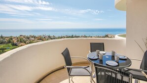 Un balcone con tavolo e sedie, affaccia su una vista costiera con edifici e mare.