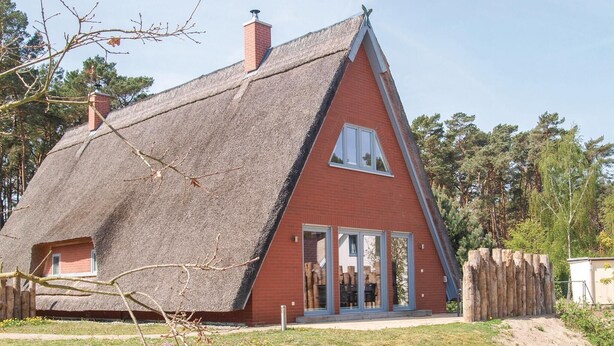 Ein Haus mit strohgedecktem Dach und roter Backsteinfassade, mit einem kleinen Fenster.