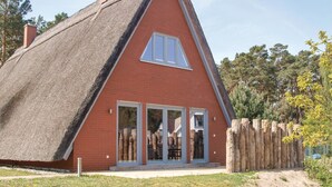 Ein Haus mit einem Reetdach, einer roten Backsteinfassade, großen Glasüren und einem Holzzaun.