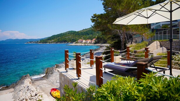 A coastal view with a lounge area, a white umbrella, and a rocky shoreline. - Gorgeous home in Crnja Luka (Crnja Luka)