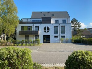A modern two-story building with a flat roof, large windows, and a circular feature on the facade.