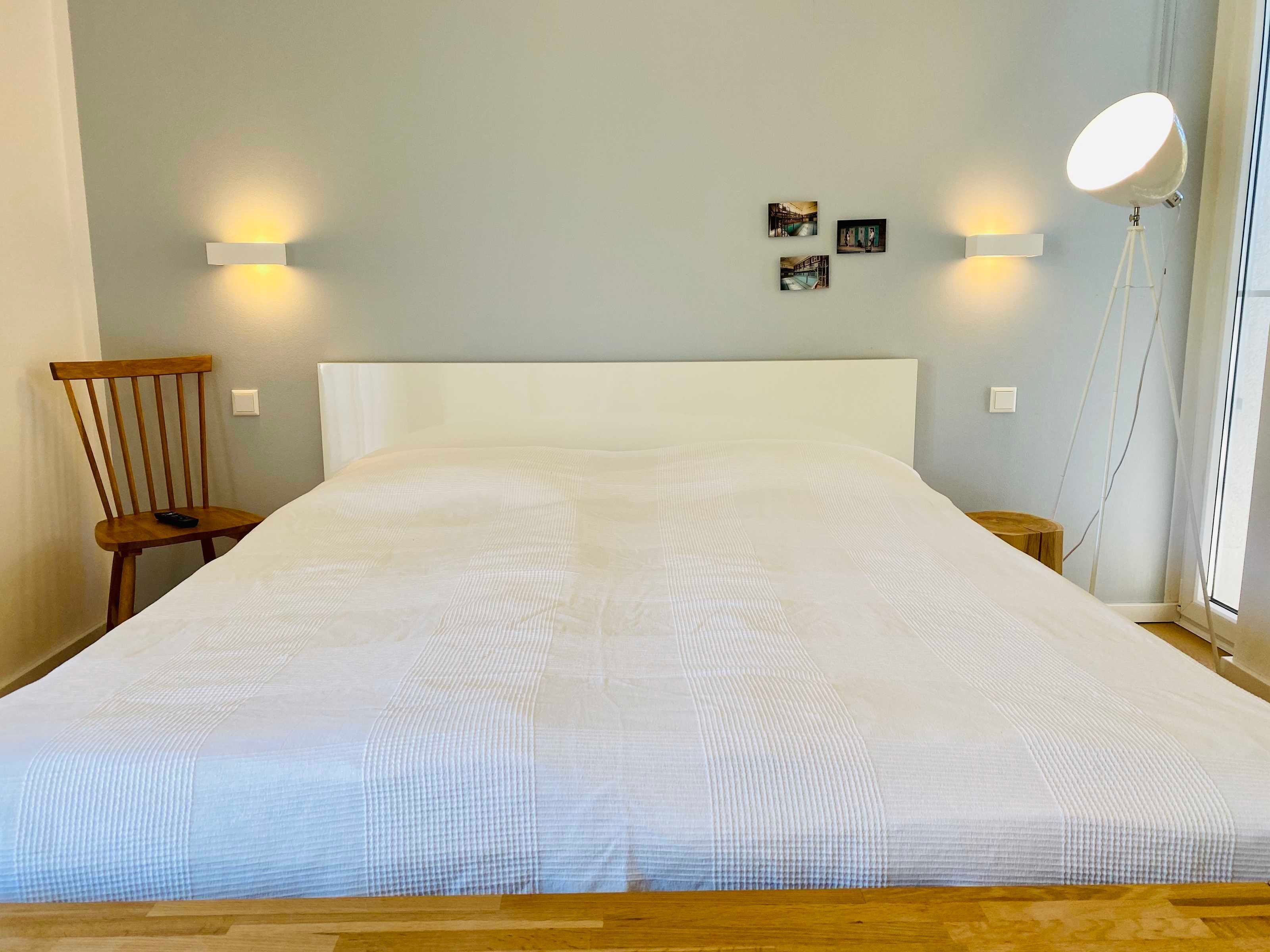 Ein Schlafzimmer mit einem großen Bett, einem Holzstuhl, zwei Wandleuchten und einem Nachttisch.