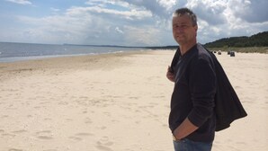 Una spiaggia con una persona in piedi, una riva sabbiosa e un cielo nuvoloso.