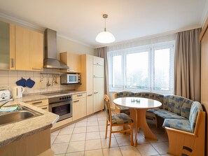 Une cuisine compacte équipée d’un four à micro-ondes, d’une cuisinière et d’un évier, ainsi qu’une table à manger avec des chaises et un banc intégré avec des coussins.