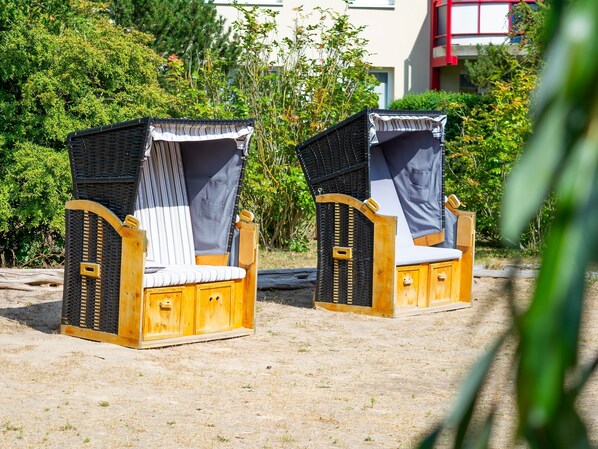 Deux chaises de plage en bois, munies de moustiquaires, sont placées sur le sable, avec en arrière-plan une végétation luxuriante.