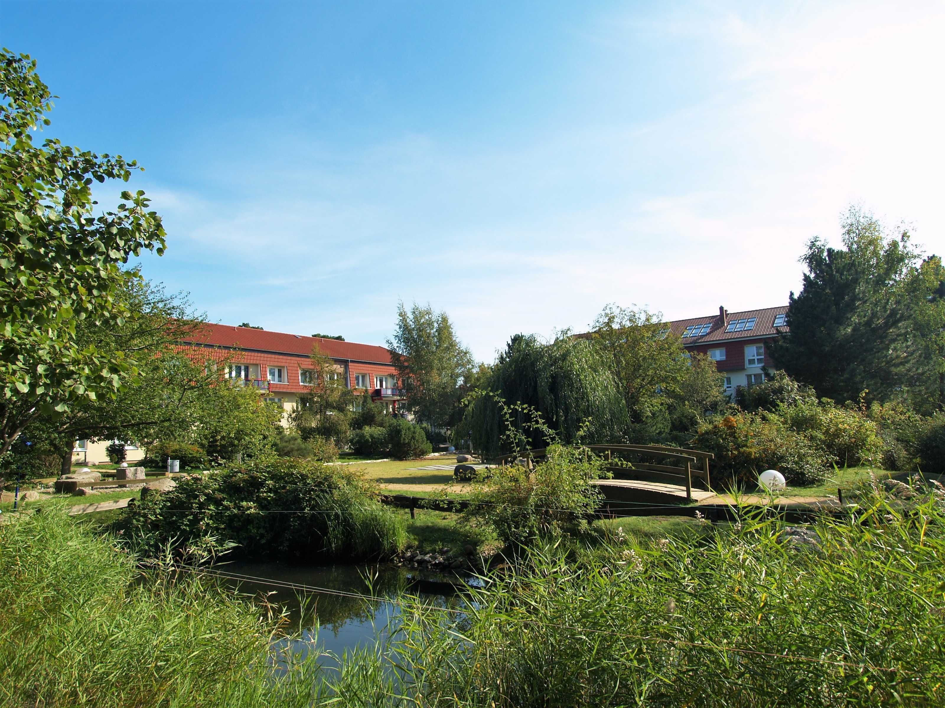 Eine friedliche Flusslandschaft mit einem Gebäude mit rotem Dach, üppigem Grün und einer kleinen Brücke.