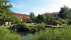Eine friedliche Flusslandschaft mit einem Gebäude mit rotem Dach, üppigem Grün und einer kleinen Brücke.