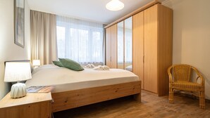Ein Schlafzimmer mit einem hölzernen Bett, einem Nachttisch, einem Sessel und einem Kleiderschrank.