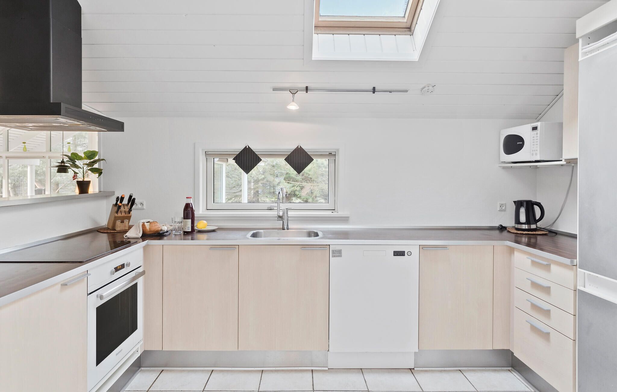 A modern kitchen with a skylight, a built-in oven, a dishwasher, and a window with a view of greenery.