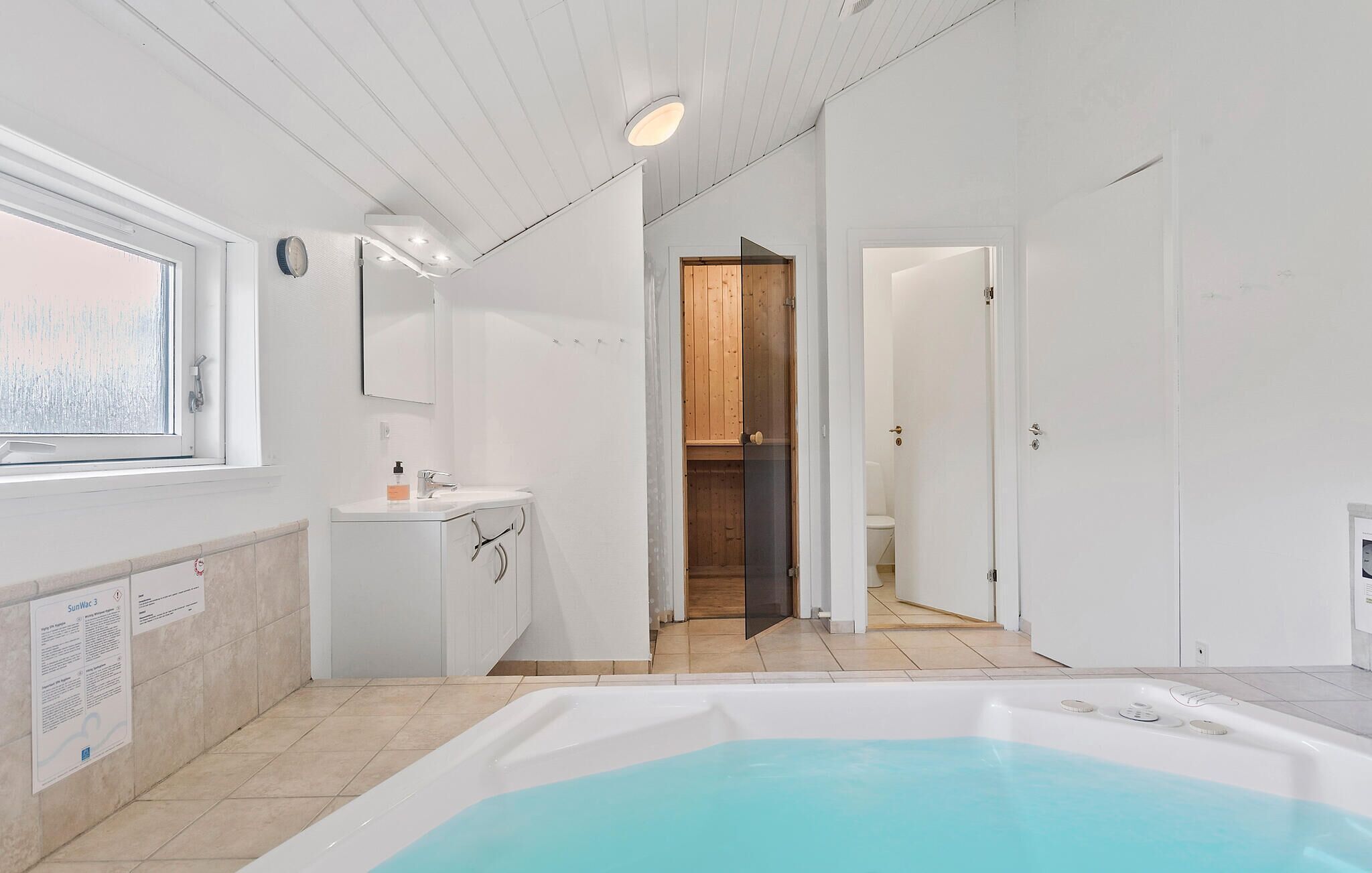 Un baño moderno con bañera, lavamanos y espejo. Hay una ventana que proporciona luz natural y una puerta que da a otra habitación.