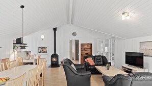 A spacious living area with a dining table, black leather sofas, a TV, and a fireplace. - Lovely home in Væggerløse with sauna (Væggerløse)