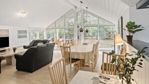 A spacious living area with a large dining table, comfortable seating, and large windows offering a view of the outdoors. - Lovely home in Væggerløse with sauna (Væggerløse)