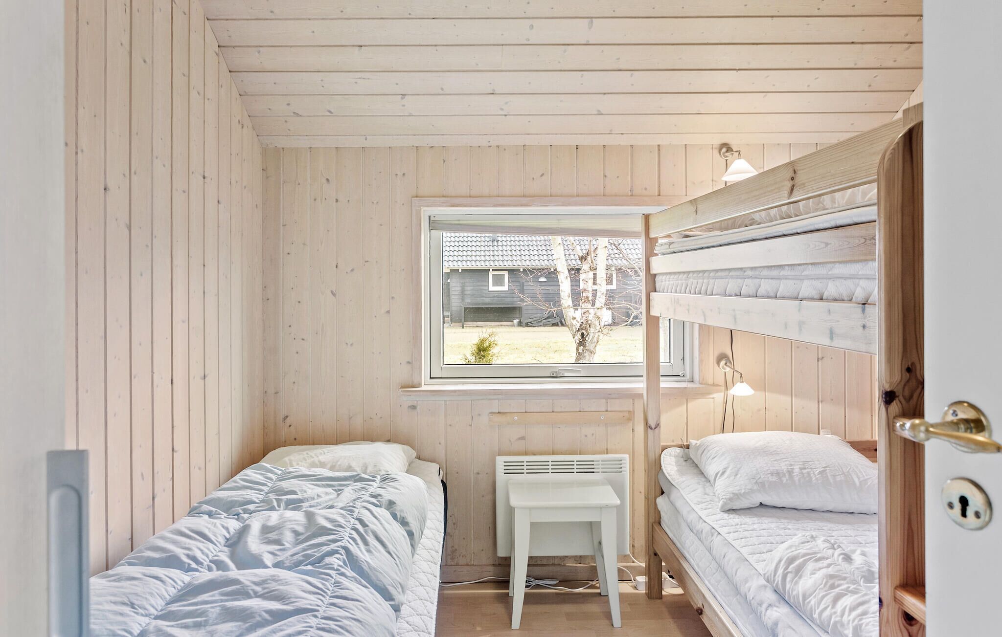 Ein kleines Zimmer aus Holz mit zwei Betten, einem Fenster und einer Heizung.
