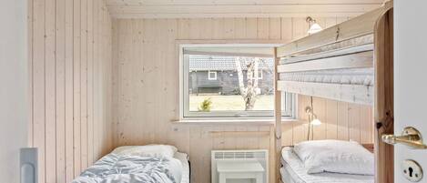 Ein kleines Zimmer aus Holz mit zwei Betten, einem Fenster und einer Heizung.