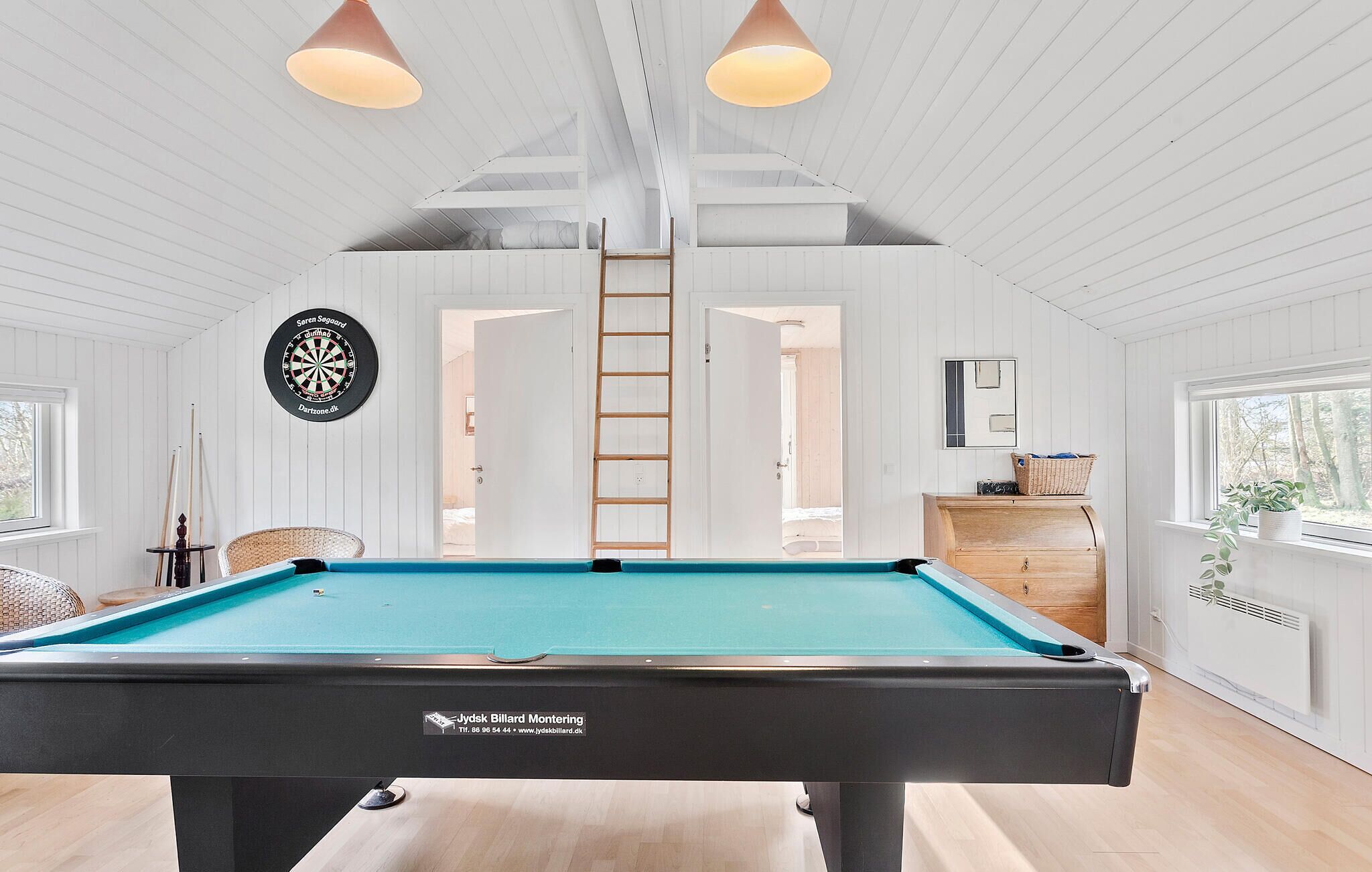 Une salle de billard équipée d’une table de billard, d’un jeu de fléchettes et d’une échelle menant à un niveau supérieur.