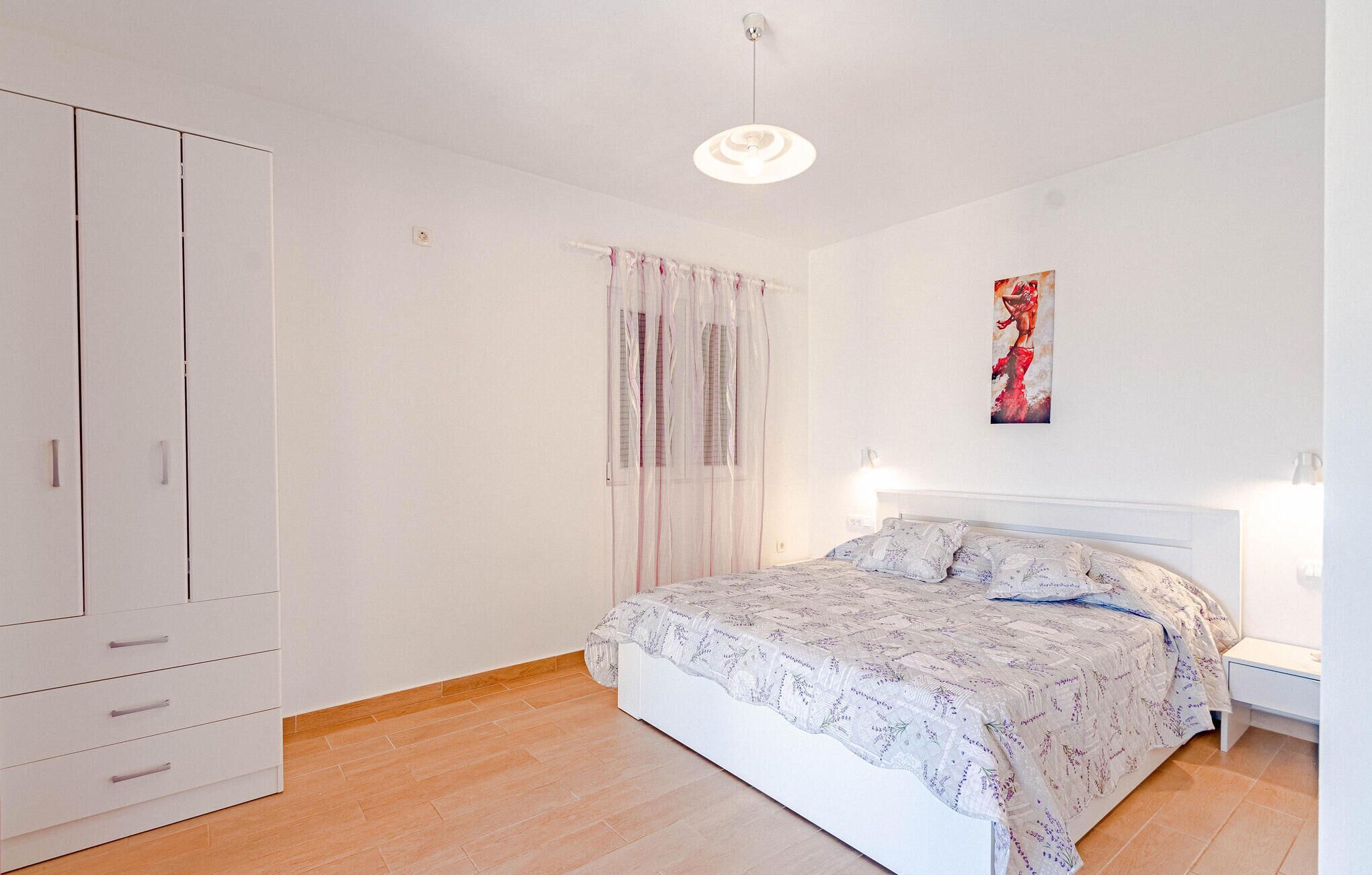 Ein Schlafzimmer mit Bett, Schrank, Fenster mit Vorhängen und einem Bild an der Wand.