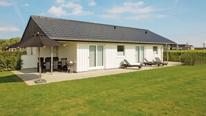 Ein Bungalow mit überdachter Terrasse, Grill und zwei Liegestühlen.