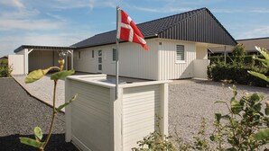Ein eingeschossiges Gebäude mit Satteldach, einer Fahnenmast mit einer Flagge und einem Schotterweg.