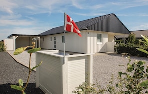 A single-story building with a sloped roof, a flagpole with a flag, and a gravel driveway. - Beautiful home in Haderslev with WiFi (Haderslev)