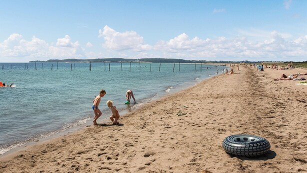 Ein sandiger Strand mit einem Reifen im Sand und Menschen, die verschiedene Aktivitäten ausüben.