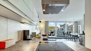 A modern kitchen with a built-in stove, a coffee machine, and a dining area with a table and chairs. - Dünenvilla 10, Whg 4 (Travemünde Priwall)