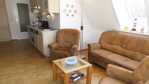 A living room with a brown sofa, a wooden coffee table with a bowl, a floor lamp, and a kitchen in the background. - 101 (BC 5) - BUE - Apartment house Hansen (Büsum)