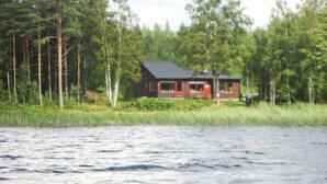 Eine Hütte mit roter Tür, umgeben von Bäumen, in der Nähe von Wasser.