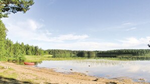 Eine friedliche Seenlandschaft mit sandigem Ufer, einem kleinen roten Boot und dichtem Wald im Hintergrund.
