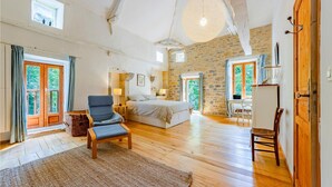 A spacious bedroom with a large bed, a chair, a desk, and a stone wall. - Gorgeous home in Caylus (Caylus)