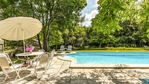 A swimming pool with a sunshade, outdoor seating, and lush greenery. - Gorgeous home in Caylus (Caylus)
