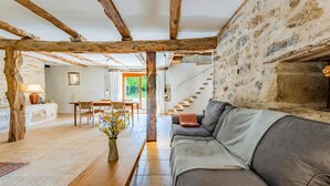 A rustic interior with exposed wooden beams, a stone wall, a sofa, a dining table, and a vase with flowers. - Gorgeous home in Caylus (Caylus)