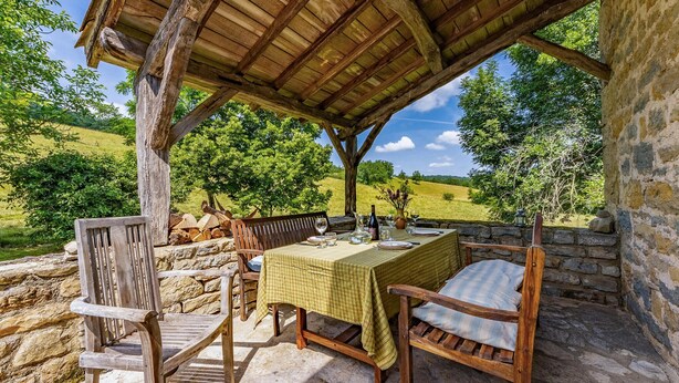 A rustic outdoor dining area with a table set for two, stone walls, and a view of a green landscape. - Gorgeous home in Caylus (Caylus)