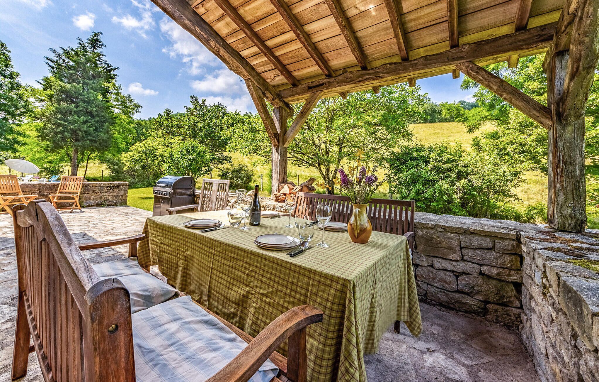 Un área de comedor al aire libre con una mesa dispuesta para dos personas, rodeada de muros de piedra y mobiliario de madera.