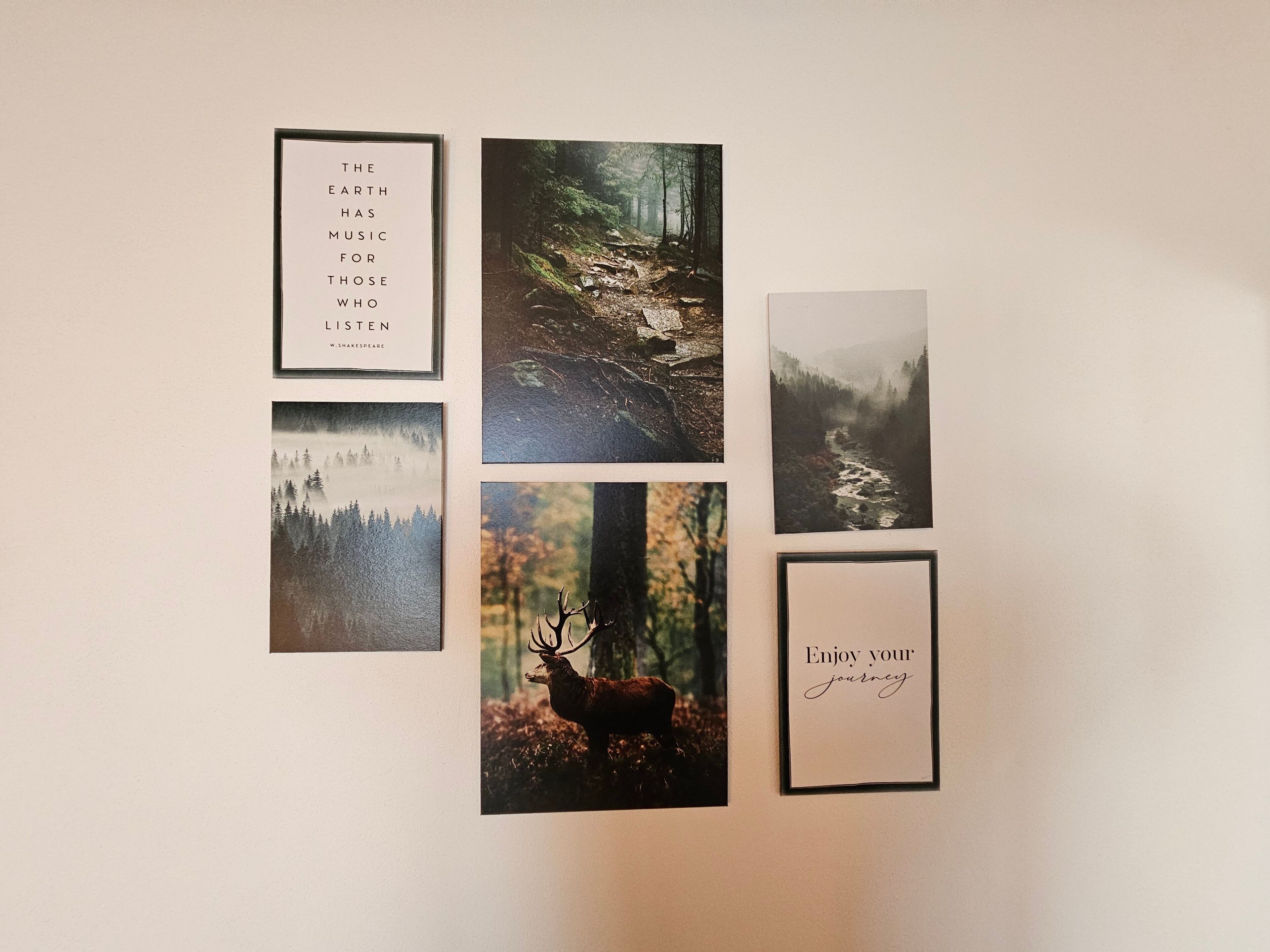 Un mur orné de divers tableaux encadrés, comprenant une citation, des scènes de forêt et un cerf.