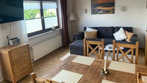 Une chambre meublée avec un canapé, une table en bois, un téléviseur et une fenêtre avec des rideaux.